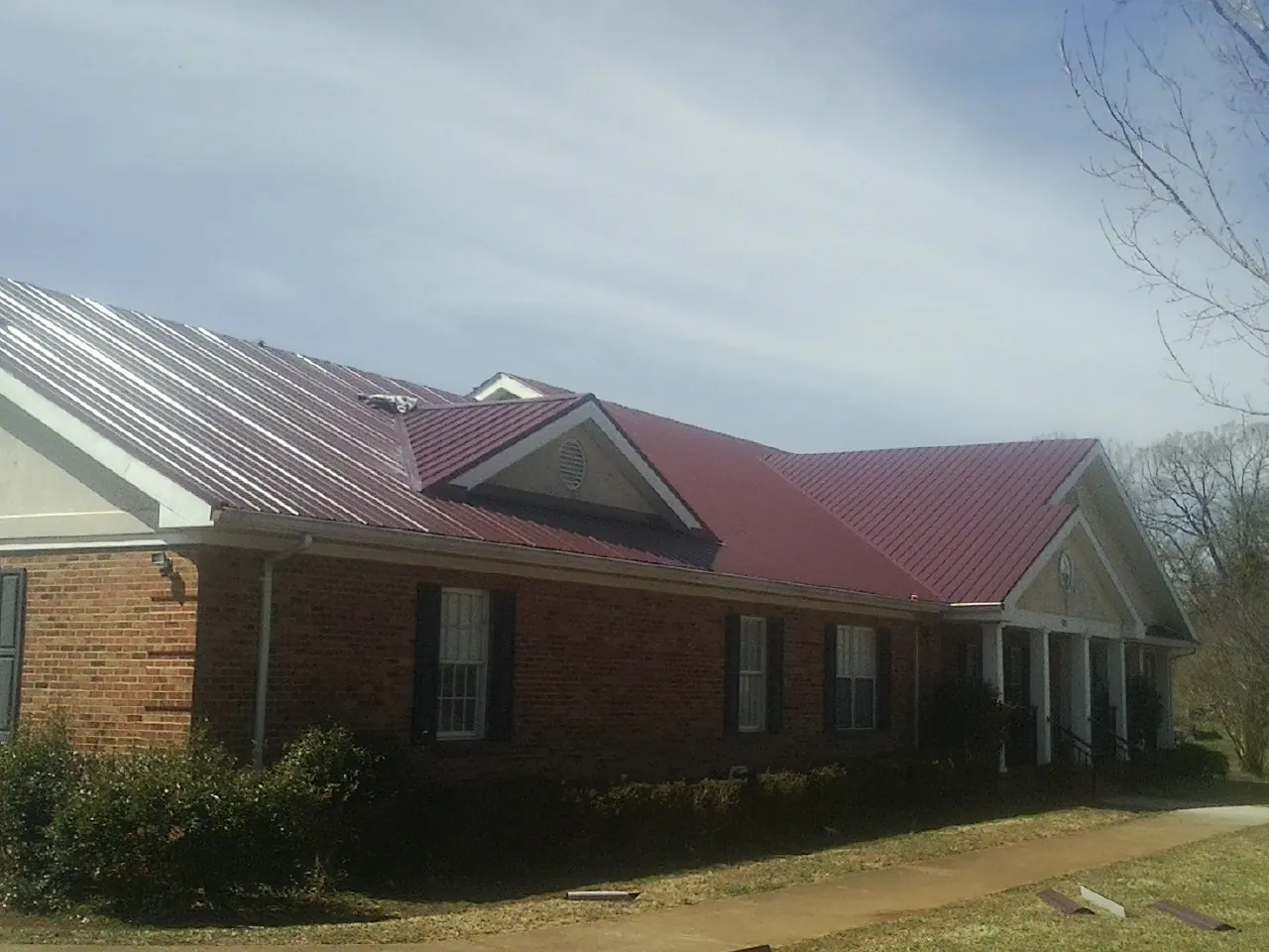 Red metal roof with gabled entries on a long brick building, from a Hail Damage Roof Repair job in Sharon