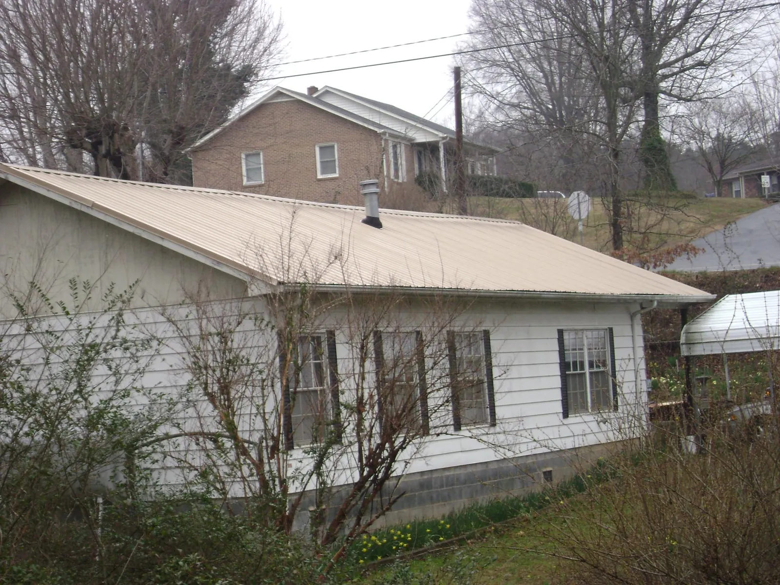 Tan metal roof on a white sided house set into a hillside — Commercial Roofing by Roofing Brothers in Sharon